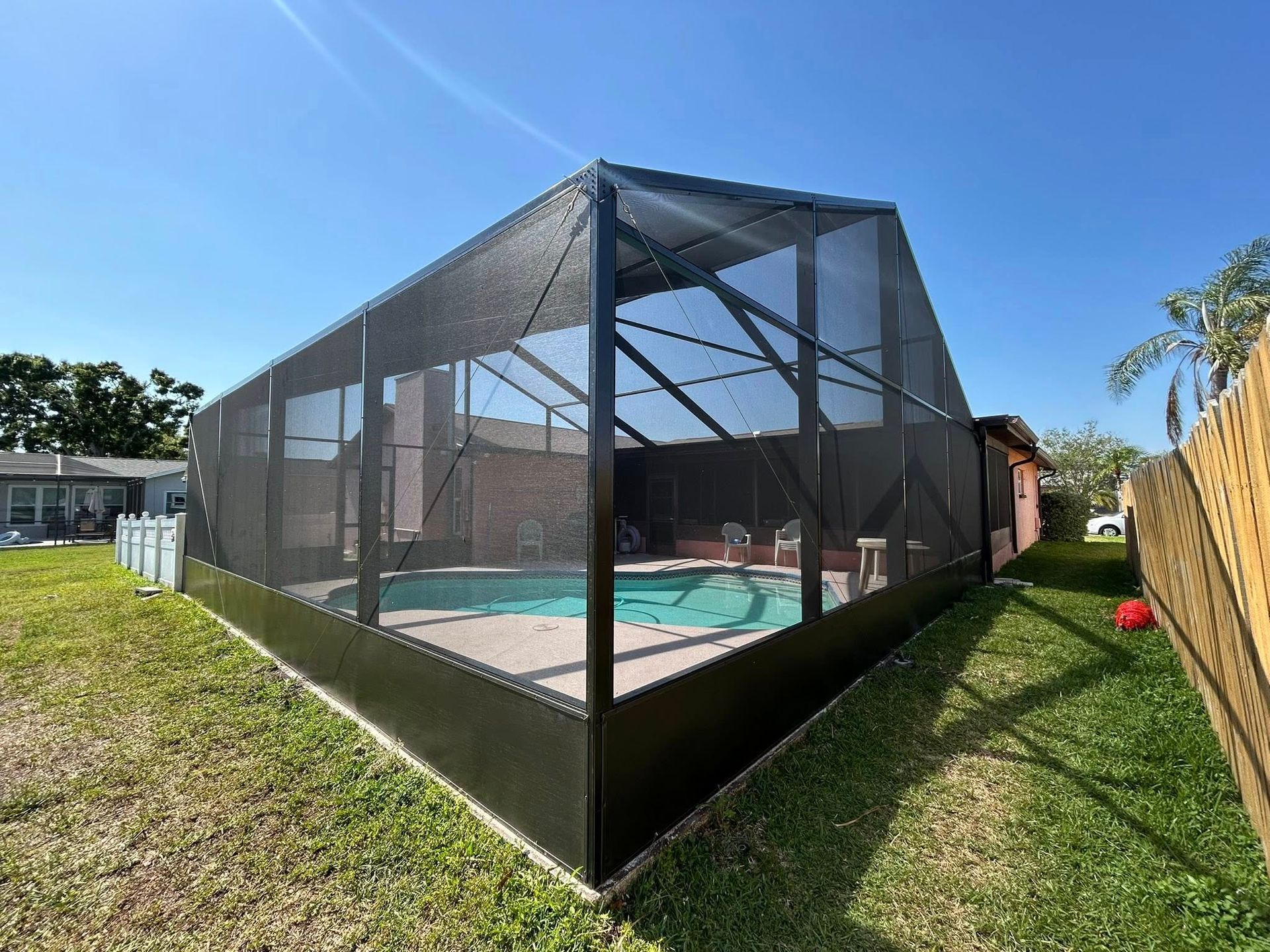 A screened-in pool enclosure on a sunny day. Black framing, pool inside, green lawn.