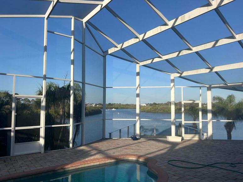 Screened-in pool enclosure overlooking a body of water with blue sky; brick patio.