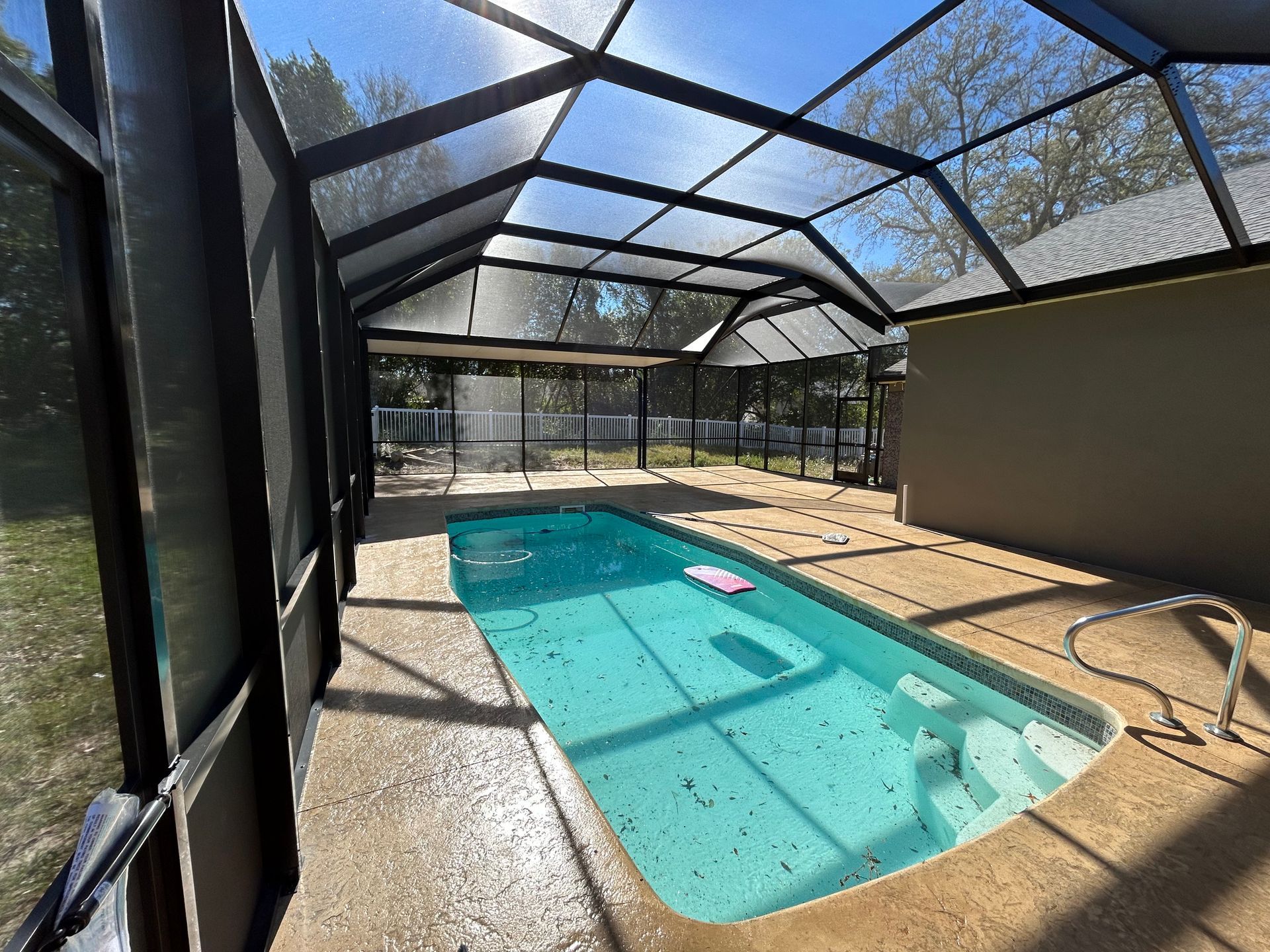 Enclosed pool with clear roof, teal water, and concrete deck. Black screened structure.