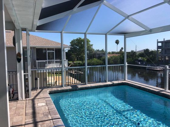 Screened-in pool area overlooking canal with blue water, surrounded by homes, under a sunny sky.