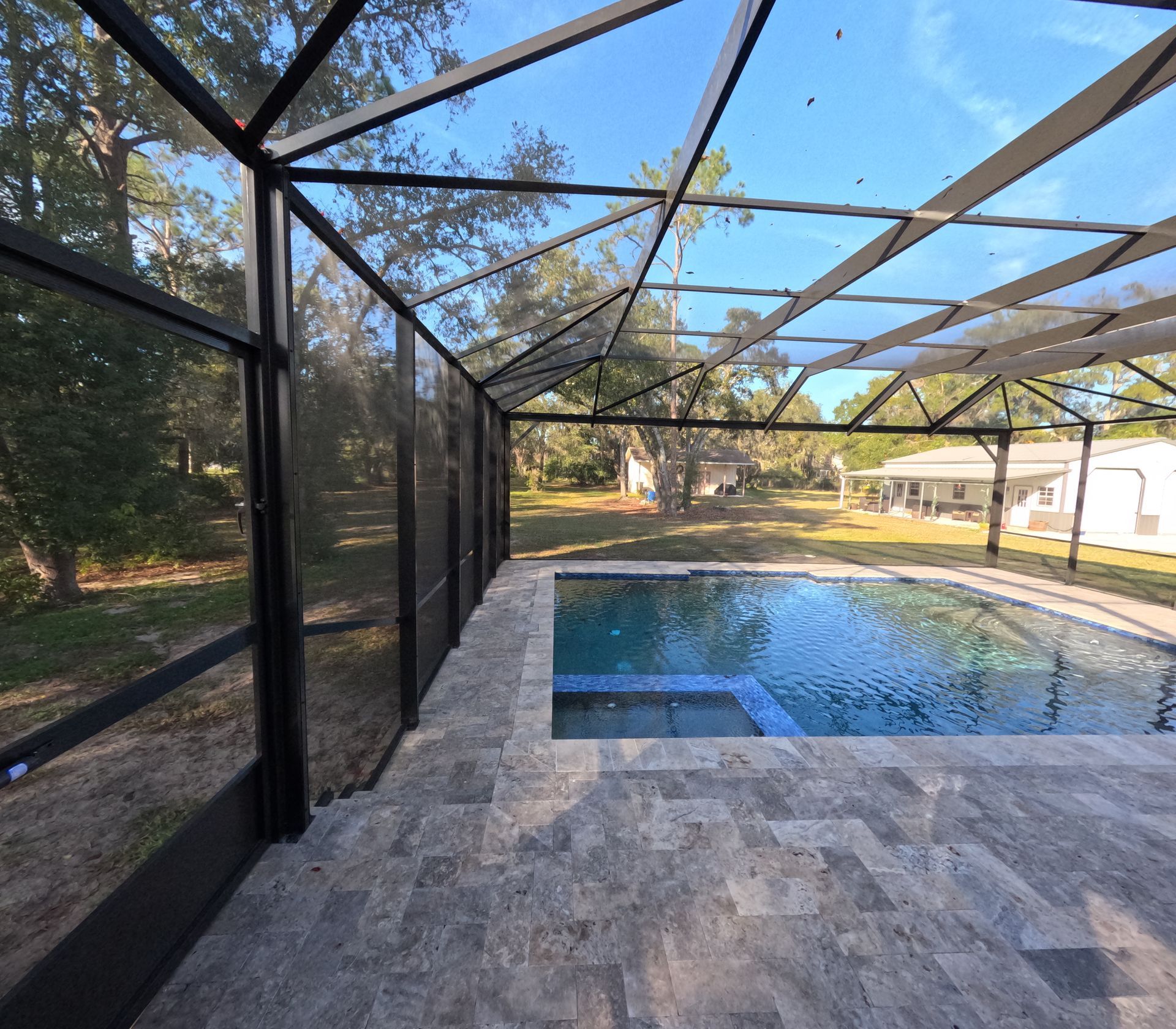 Pool enclosure with a screened roof and patio overlooking a pool and yard on a sunny day.