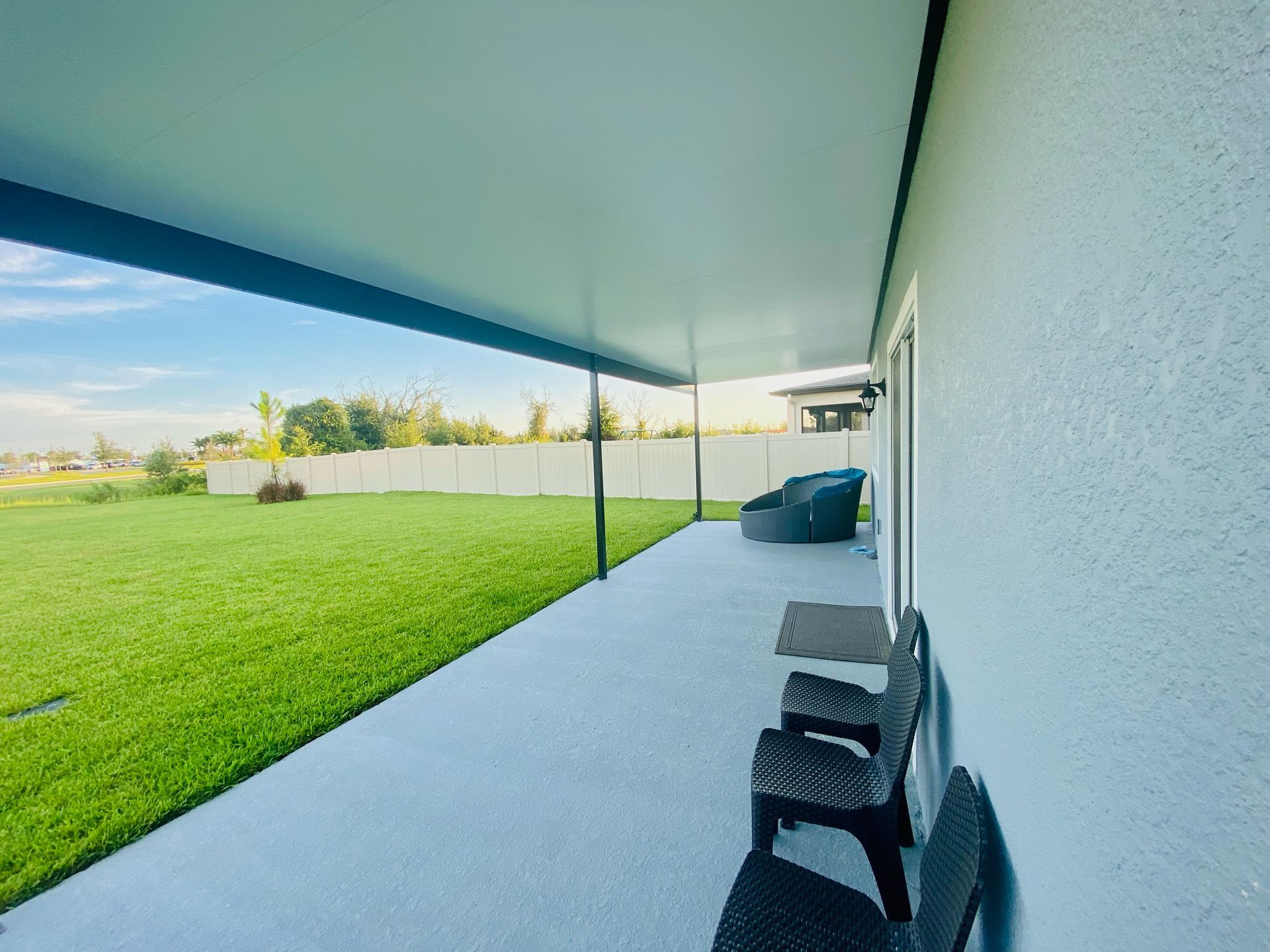 Covered patio with chairs, overlooking a green lawn and white fence.