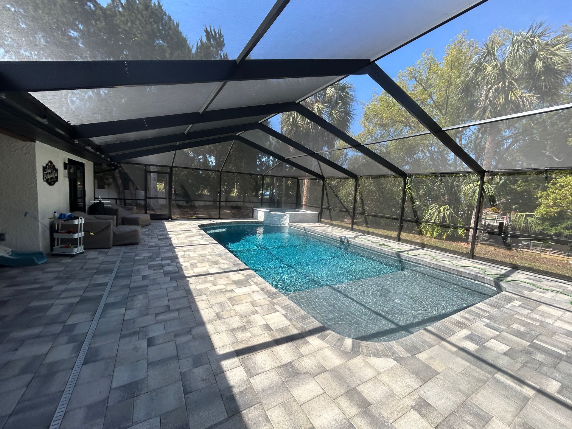 Pool enclosure with a rectangular pool, gray pavers, and a sunny sky.