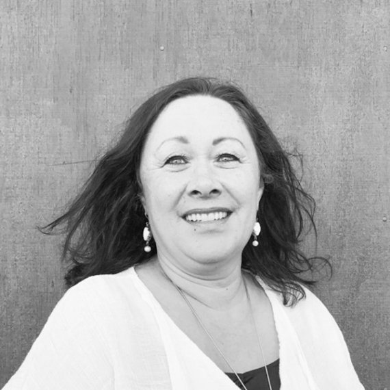 Smiling woman with dark hair in a white cardigan against a wooden wall