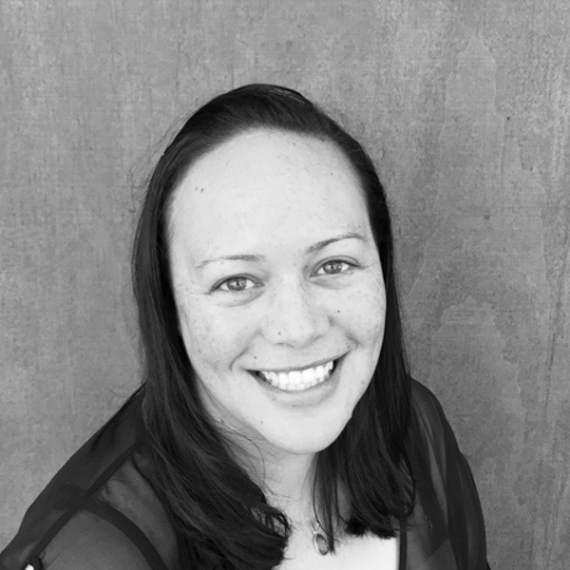 Smiling person with shoulder-length dark hair against a plain gray background