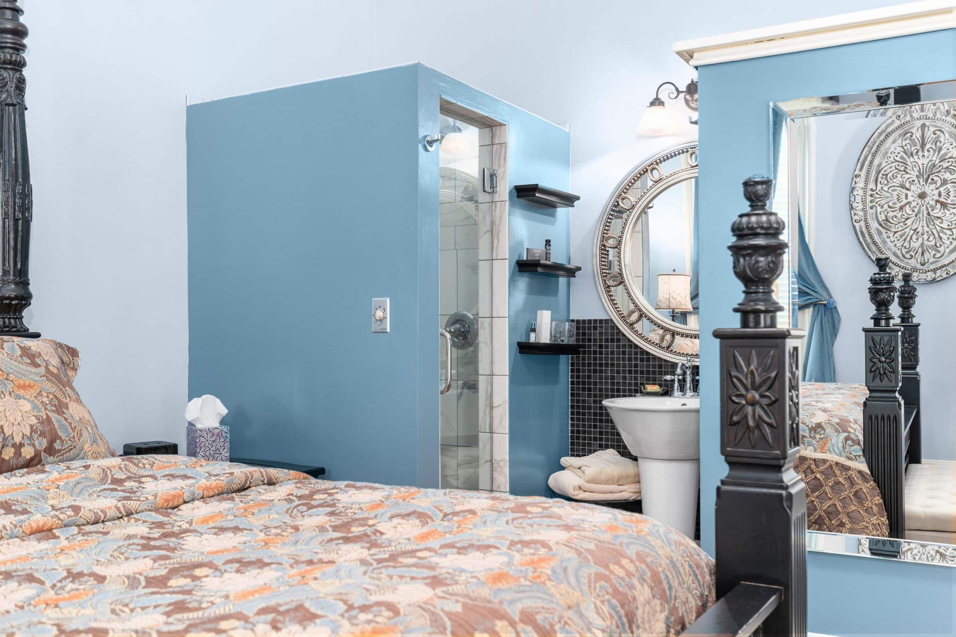 A bedroom with a four poster bed , a sink and a mirror.