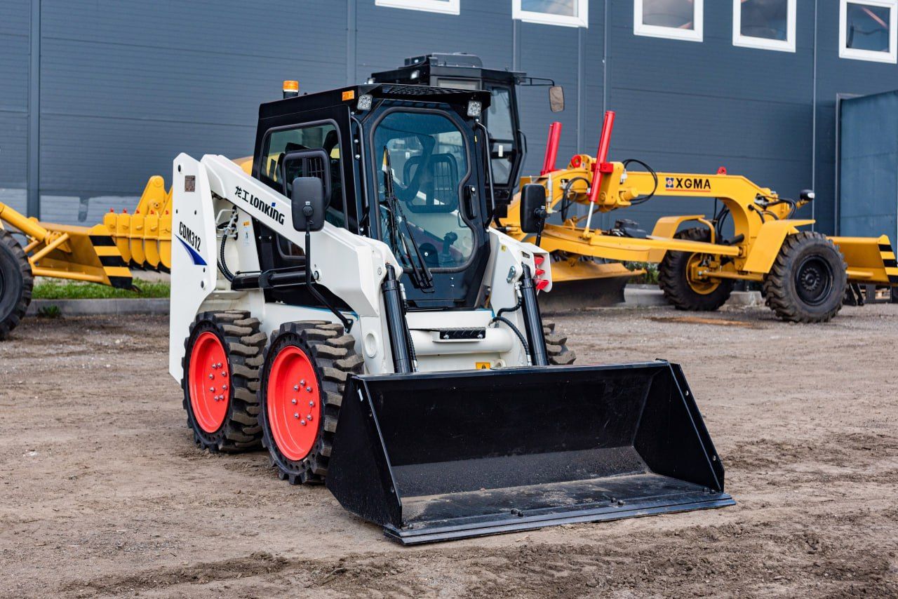 White Bobcat skid-steer loader with a black bucket, orange wheels, and a yellow grader in the background.