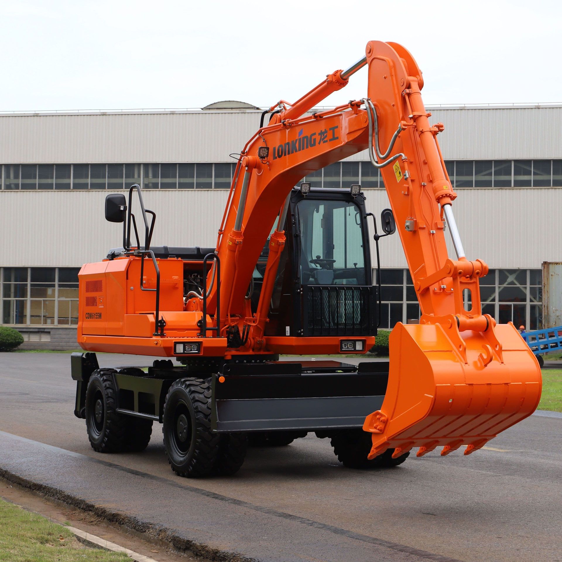 Orange wheeled excavator on paved road near a building.