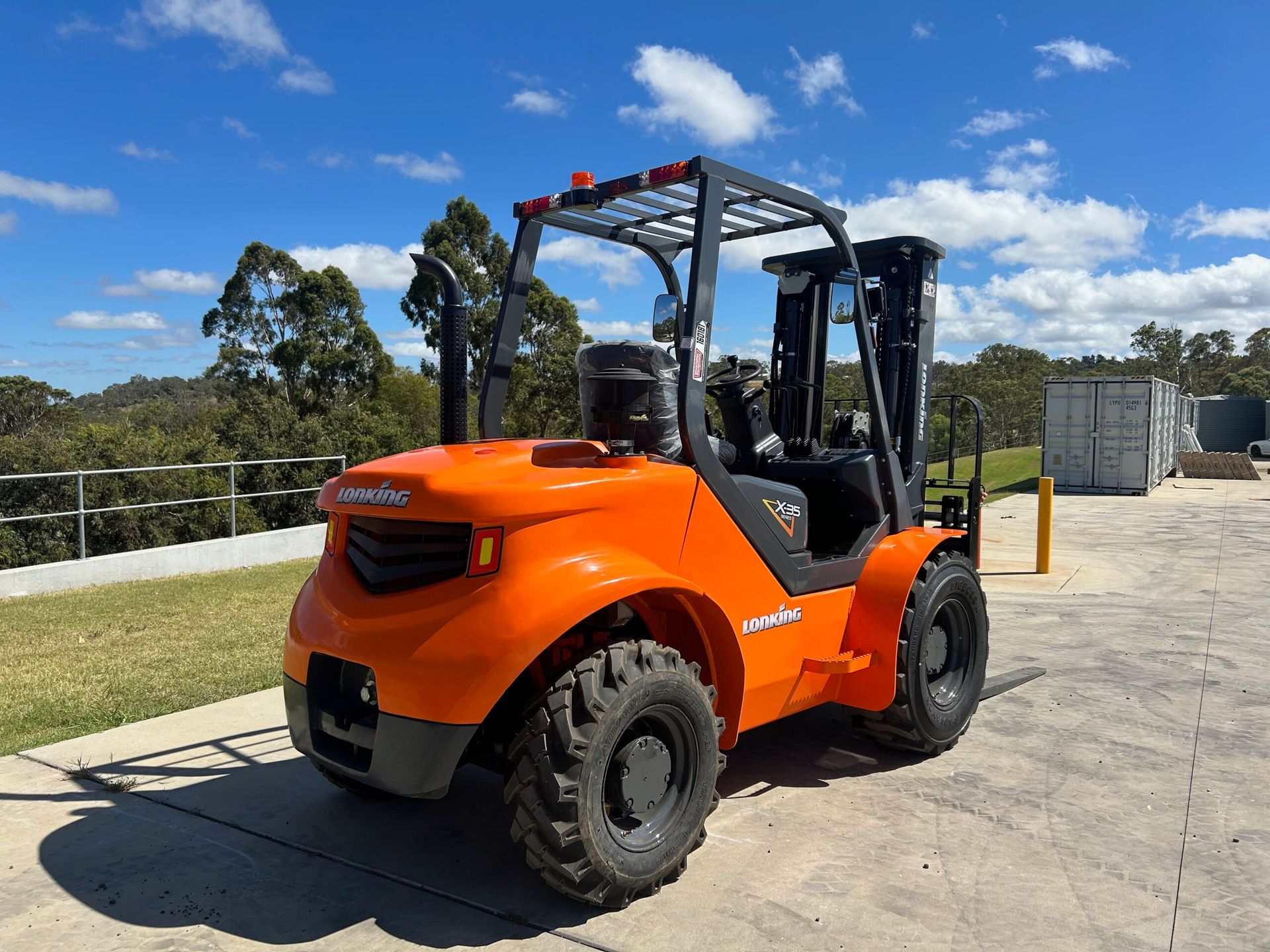 Orange forklift with black wheels outdoors on a sunny day.