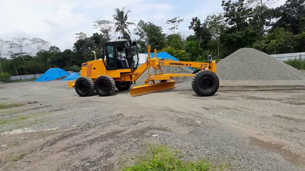 Yellow motor grader grading gravel in an outdoor setting.