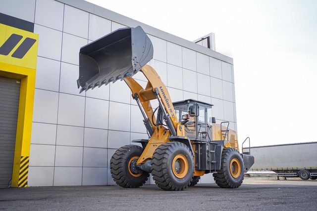 Yellow front-end loader with raised bucket in front of a gray industrial building.