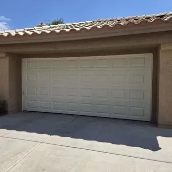 Two-car wooden garage doors on a suburban house with a light green exterior and driveway