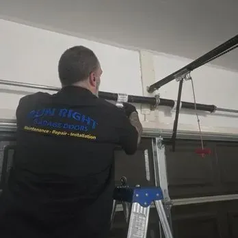 Gloved hand spraying lubricant onto a garage door opener chain and rail