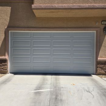 Two-car garage with white doors and a brick driveway in front of a house