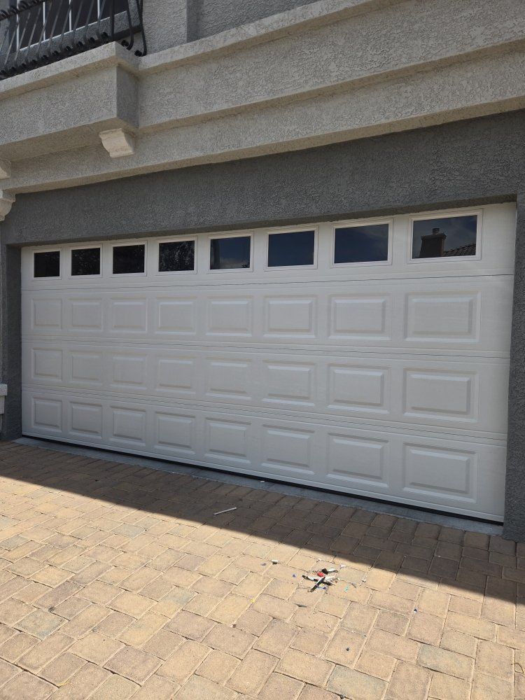 Light gray double garage door on a stone house with a shingled roof and paved driveway