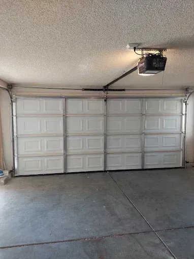 Open garage door with white insulated panels and metal tracks overhead