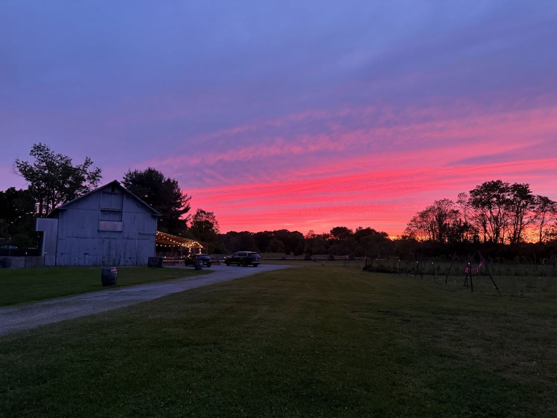 Sunset over a grassy field beside a small building, with pink and purple clouds in the sky