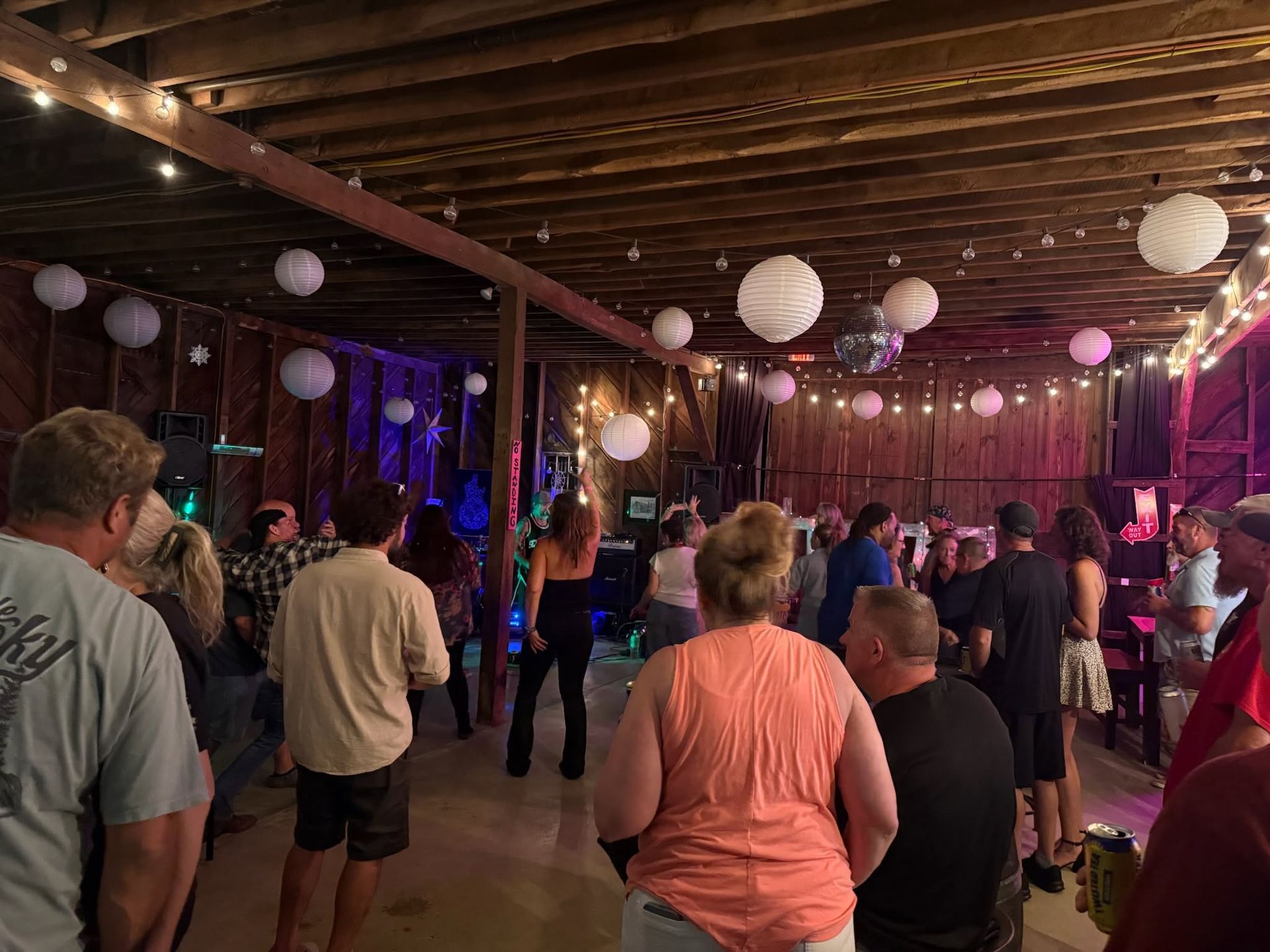People standing and dancing in a dimly lit indoor party space with hanging lanterns and colored lights.