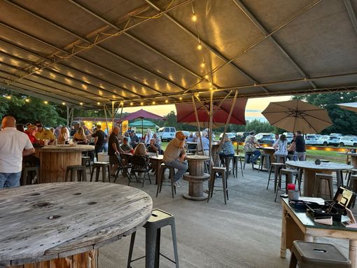 Open-air restaurant patio at dusk with people seated under string lights and umbrellas