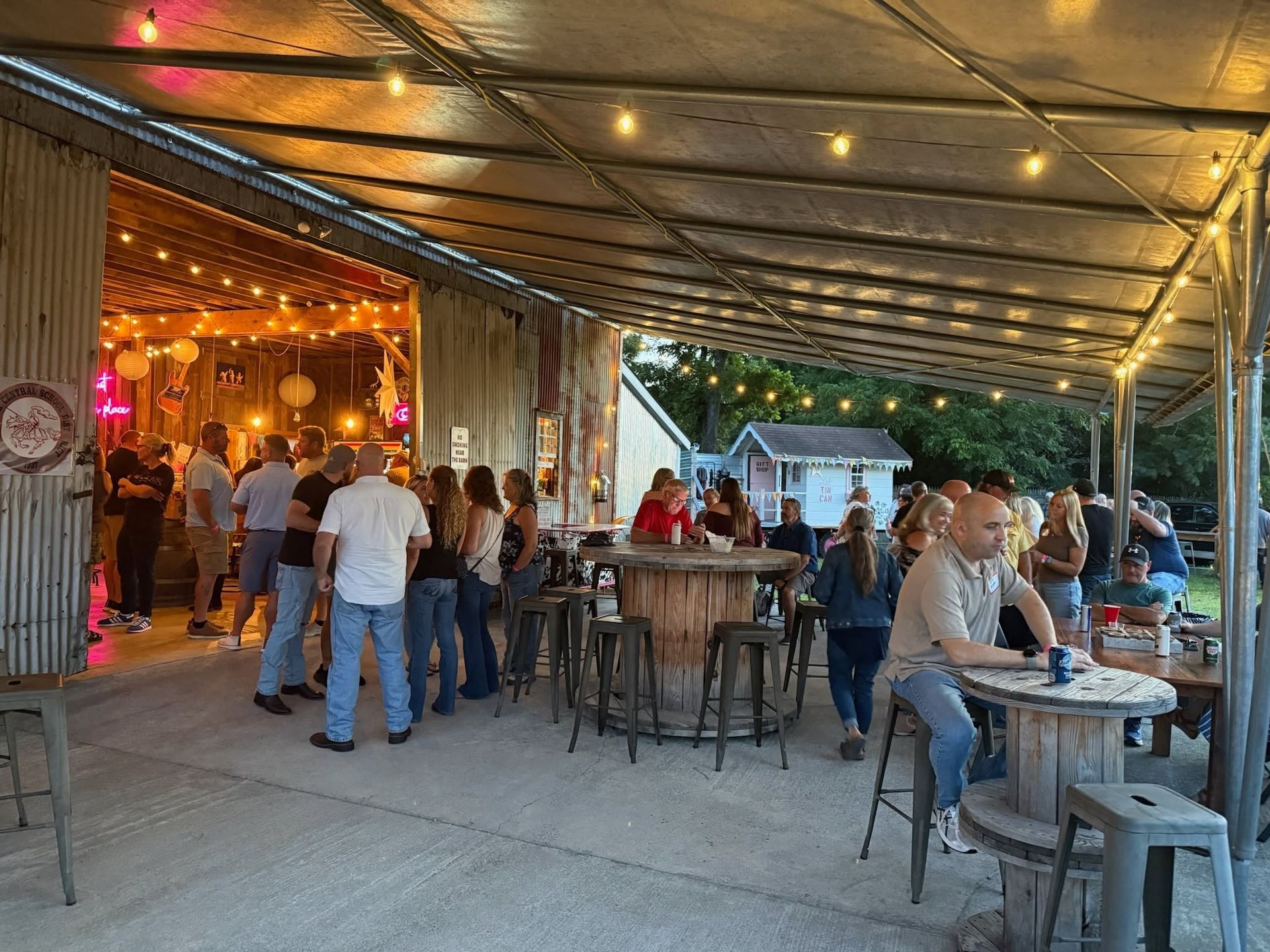 Covered outdoor restaurant patio with people dining at tables under warm string lights