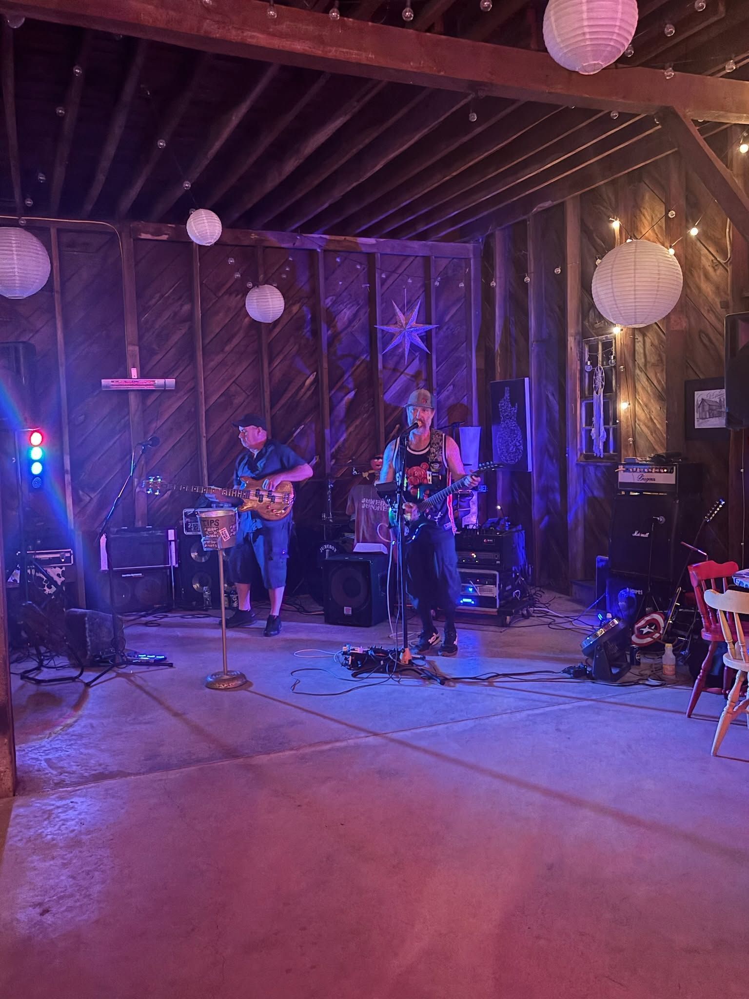 Live band performing on a dimly lit stage with purple lighting and hanging paper lanterns.