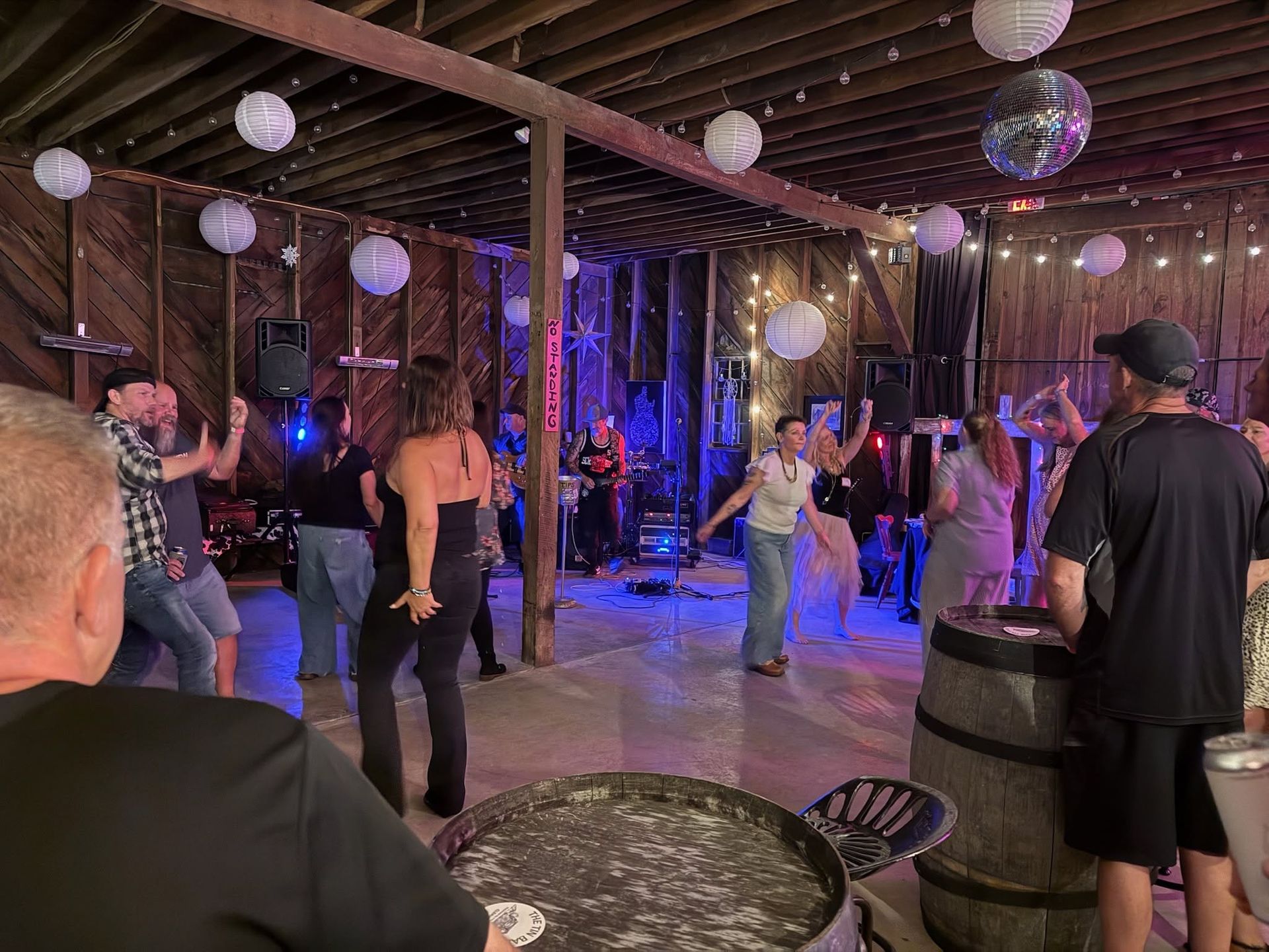 People dancing in a rustic indoor venue with hanging lanterns and a live band stage.