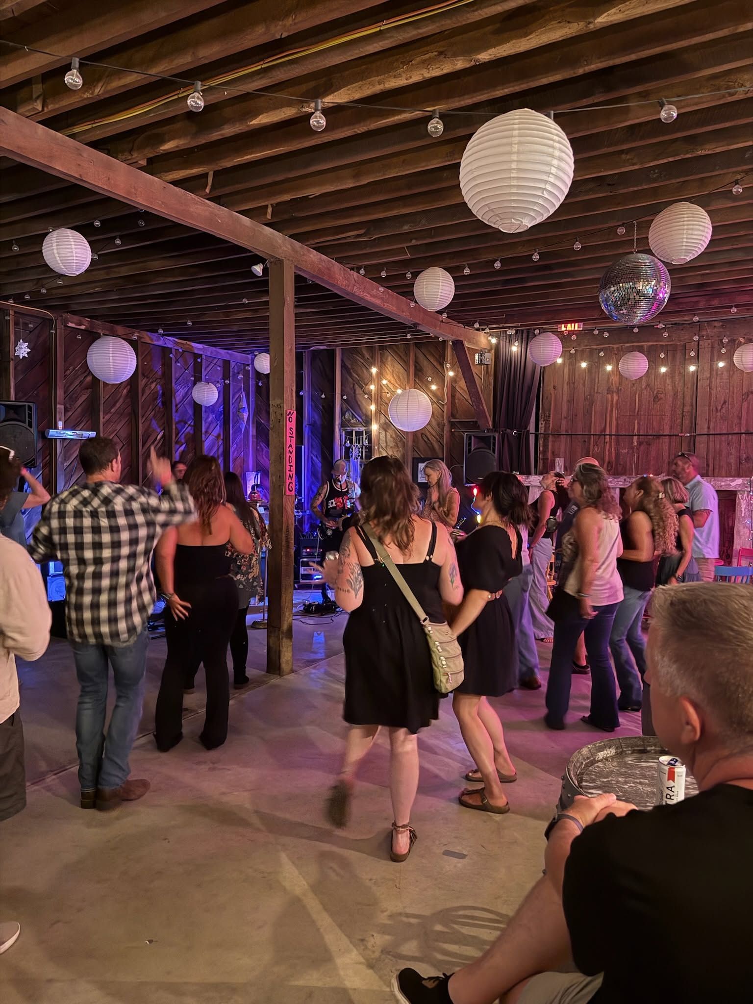 People dancing at an indoor party under hanging paper lanterns with purple lighting.