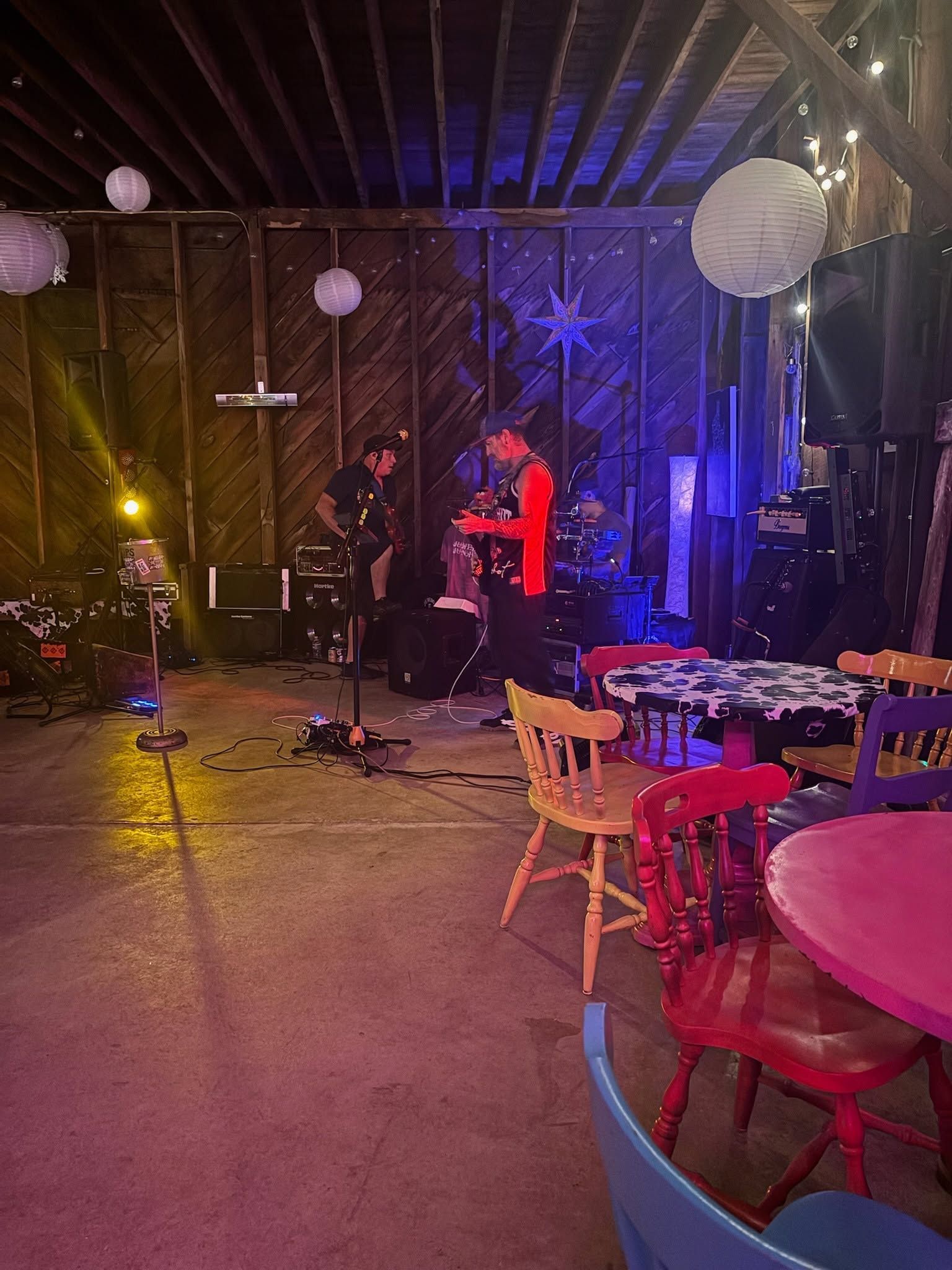 Dimly lit event space with hanging lanterns, string lights, and red and pink tables and chairs.