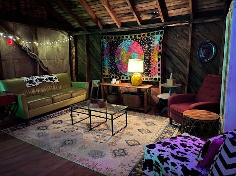 Cozy rustic lounge with sofas, rug, coffee table, colorful wall hanging, and warm lamp lighting