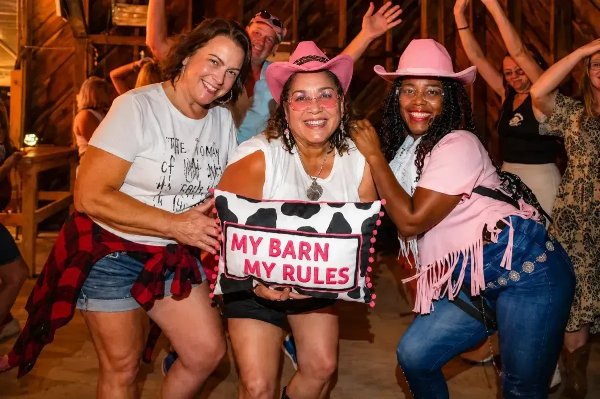Three people posing with a sign that says “MY BARN MY RULES” at a lively party.