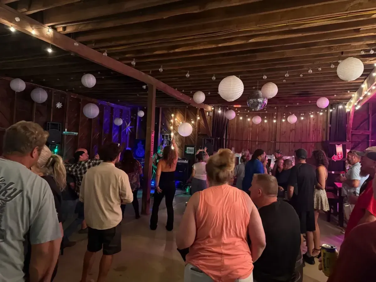 People standing and dancing in a dimly lit indoor party space with hanging lanterns and colored lights.
