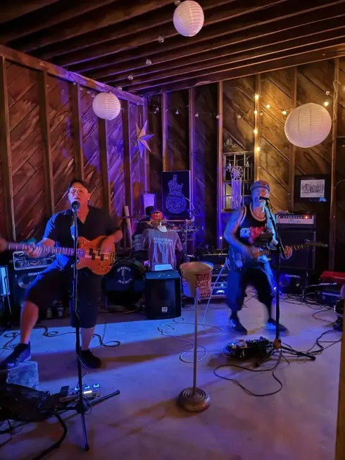 Three musicians performing onstage in a rustic wooden venue under warm hanging lights.