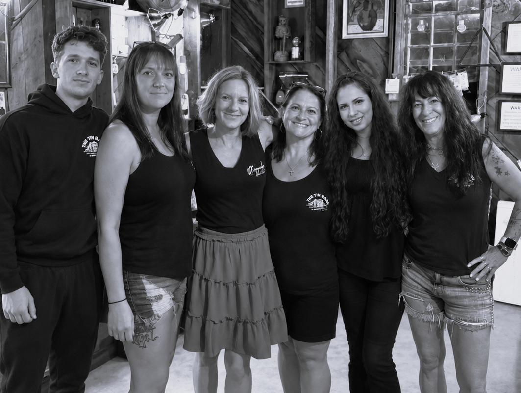 Group of nine people in black shirts and jeans posing against a corrugated metal wall.