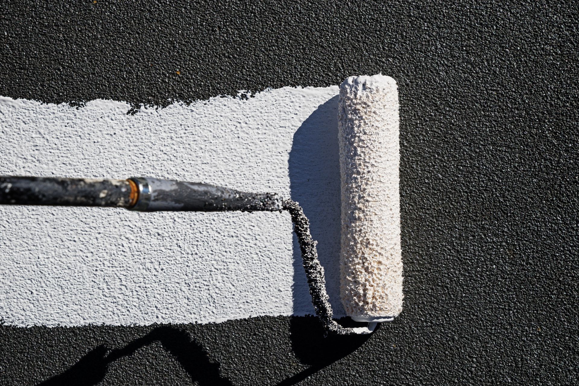 Paint roller applying a white sealant onto a dark surface.