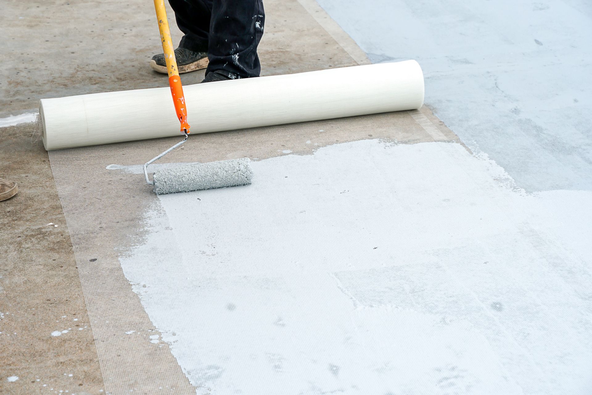 Worker rolling white waterproofing coating onto a flat roof surface.