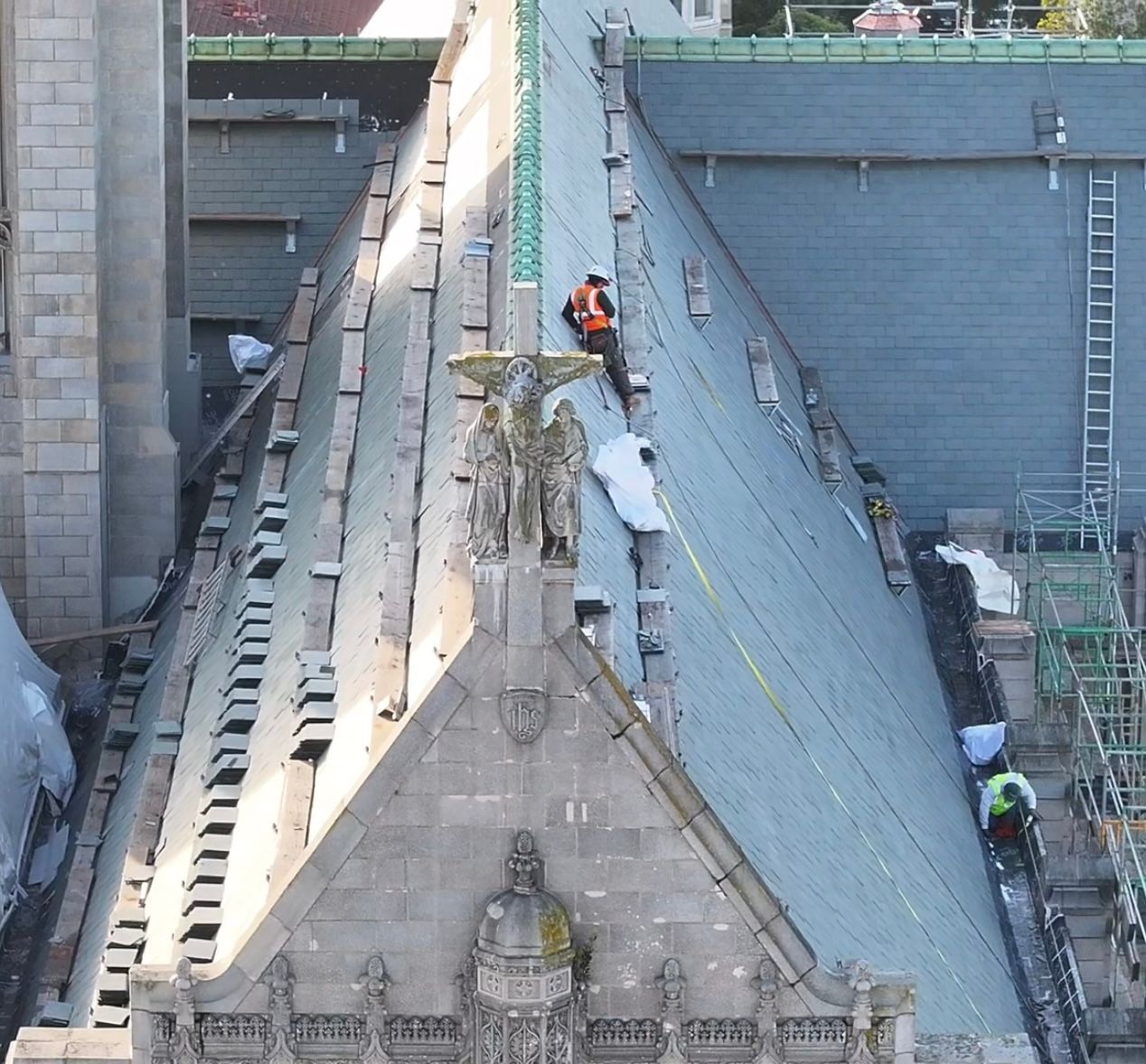 Workers on a sloped roof with scaffolding, replacing the green tiles. Decorative statues adorn the facade.