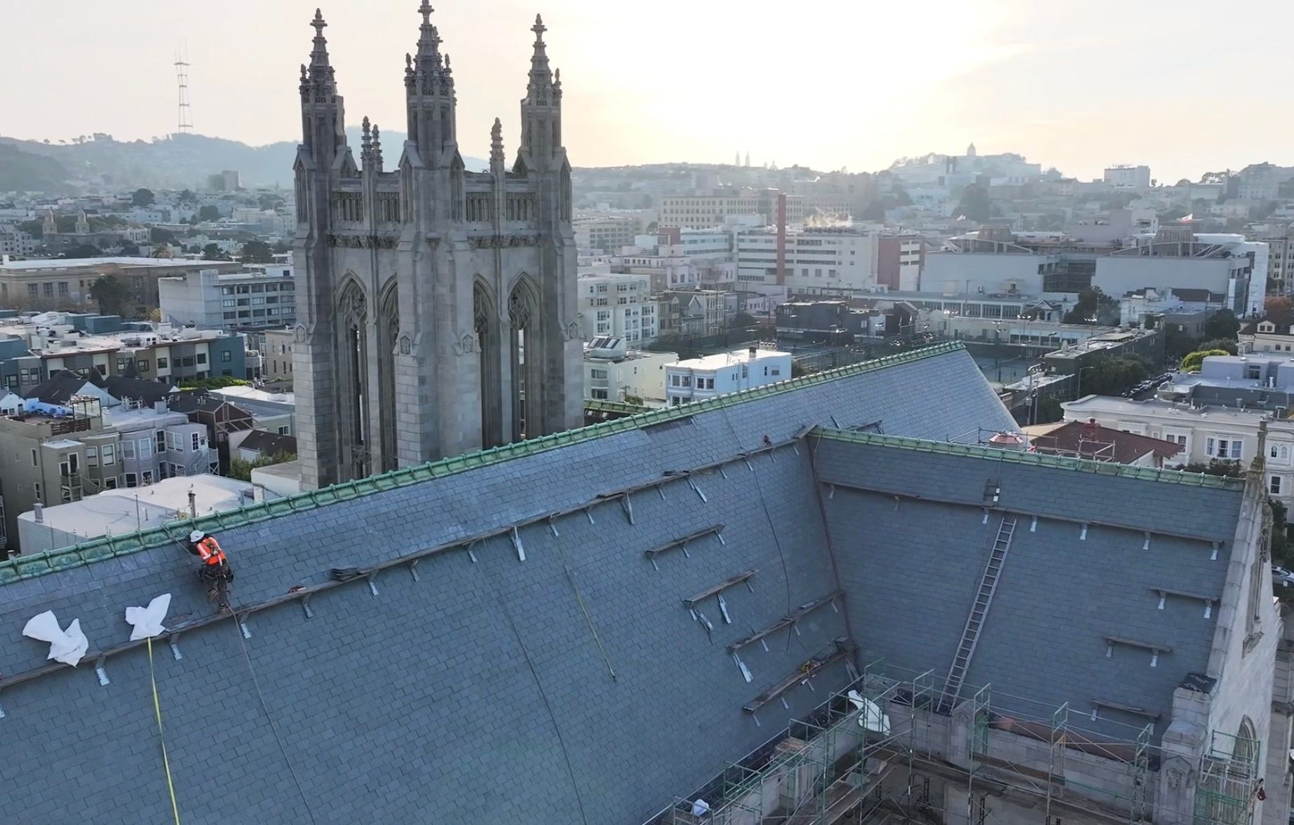 Roofer on cathedral roof with tall spires, cityscape background, sunny day.