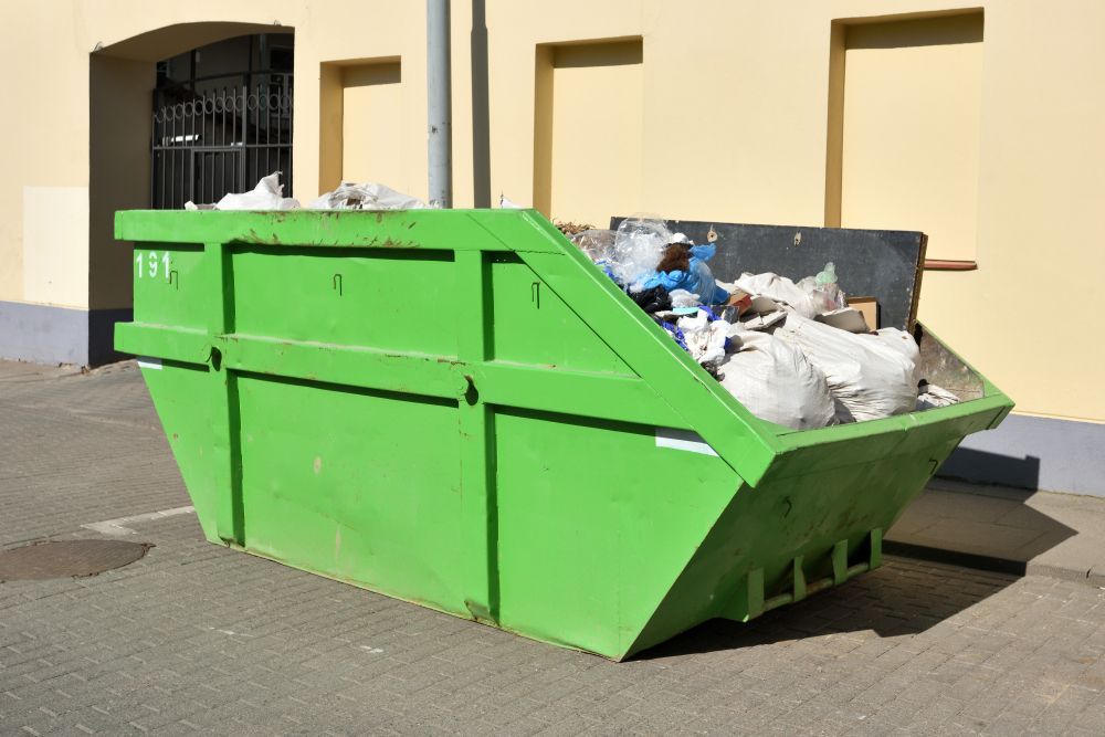 Green Dumpster Overflowing With Trash Near a Building — All Suburbs Garden Bags in Redlynch, QLD