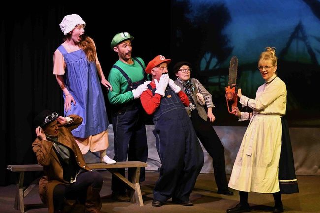 A theatrical scene: People dressed as Mario characters, one with a chainsaw, in a stage setting.