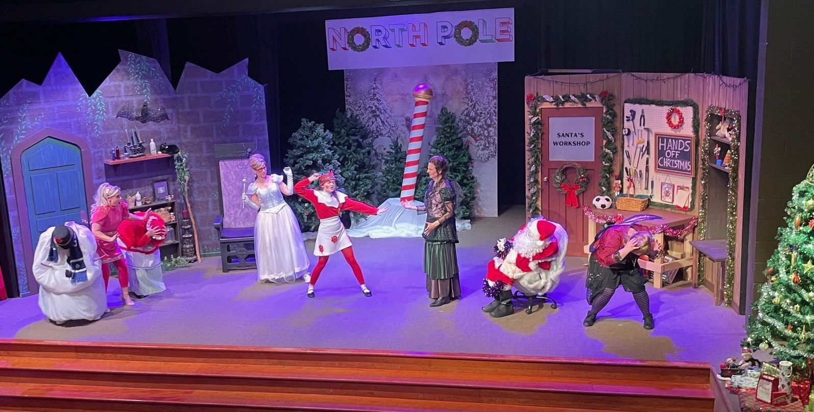 A stage production of Christmas characters in colorful costumes, with props and a decorated tree.