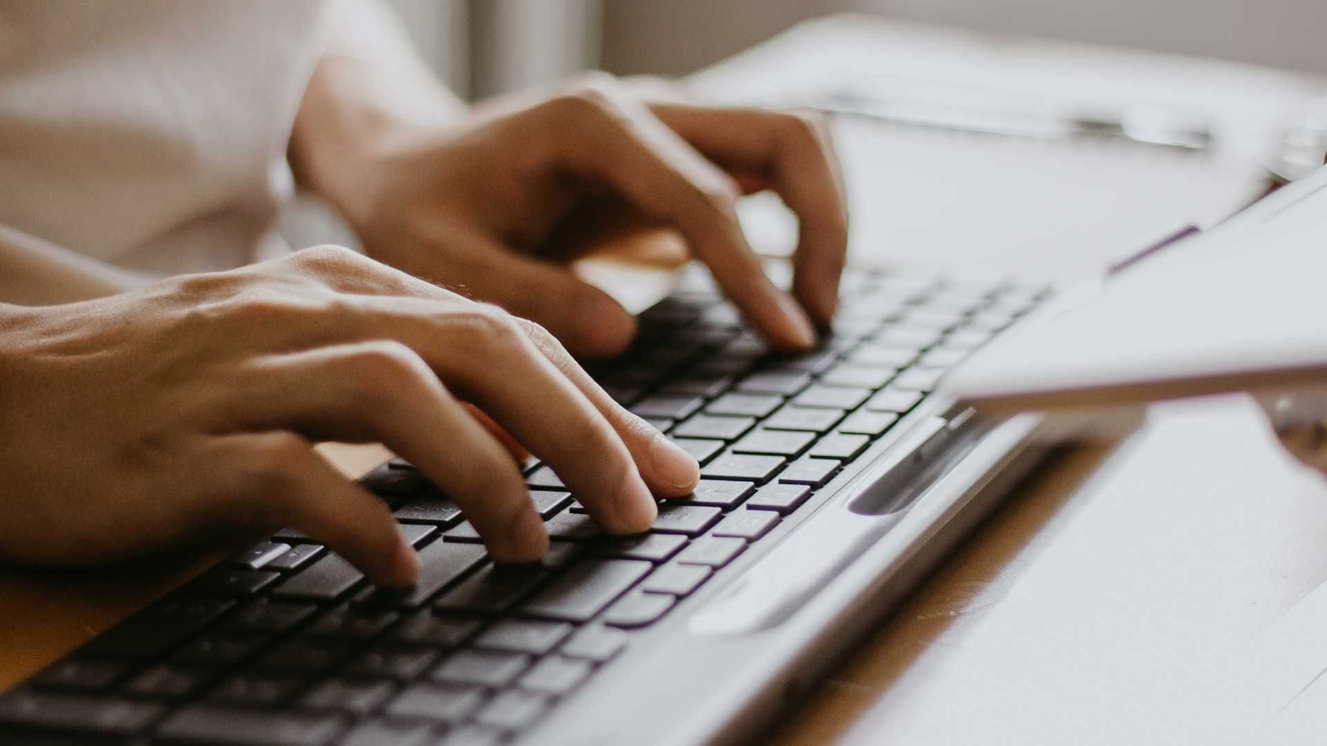 Hands typing on a laptop keyboard beside a notebook