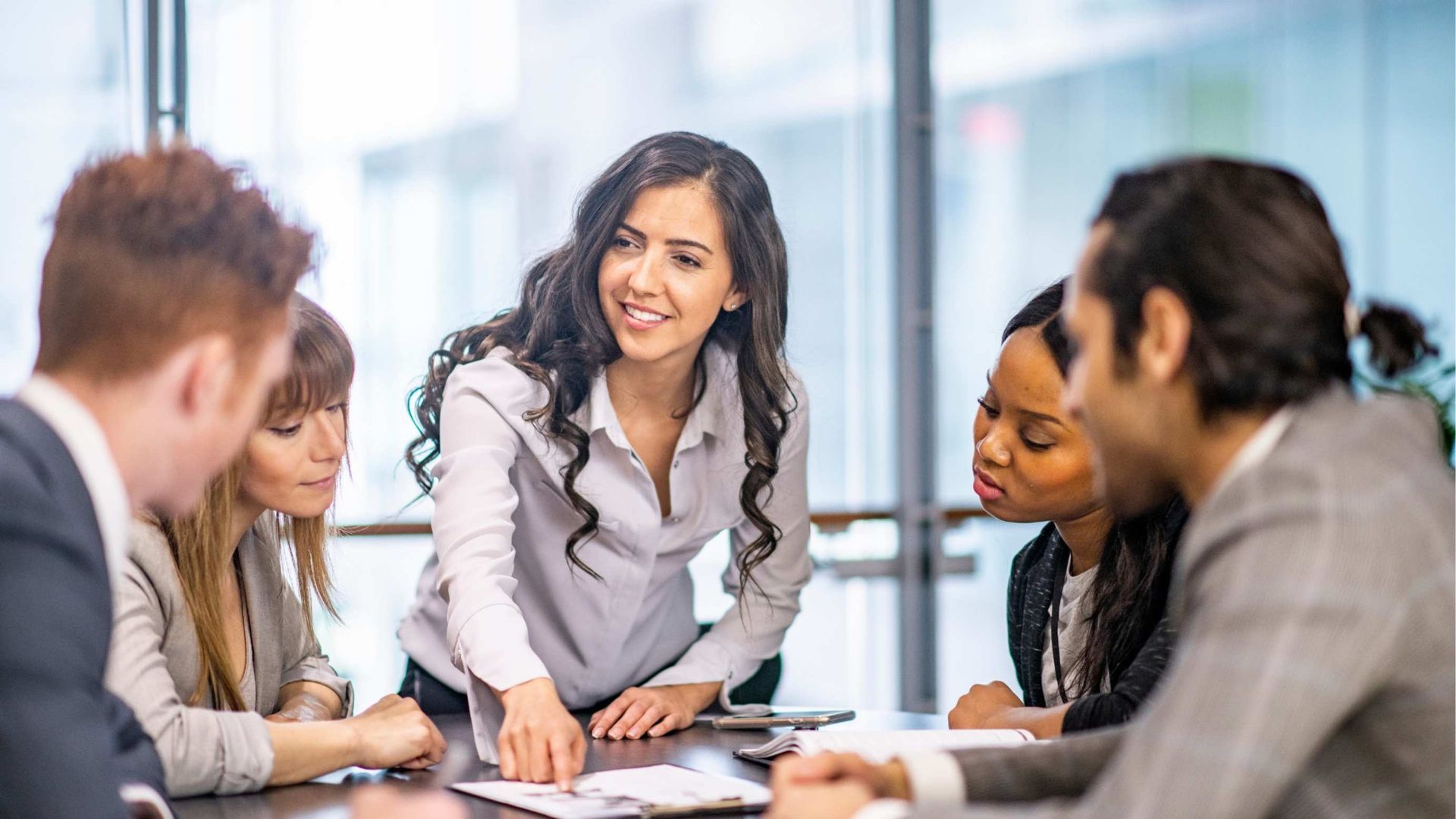 Four coworkers in a meeting, with one woman speaking and others listening around a table.