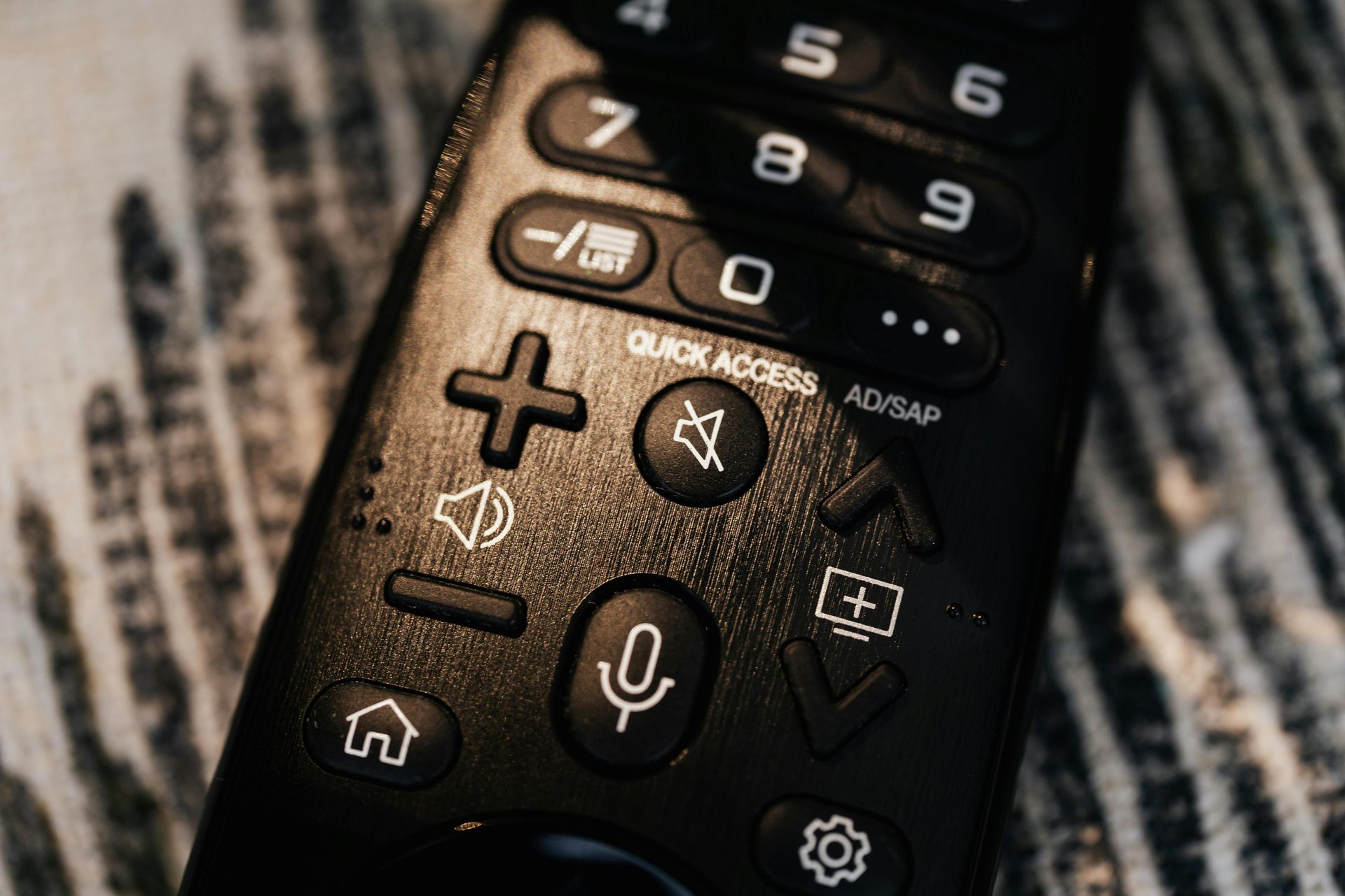 A close up of a black remote control on a wooden table.