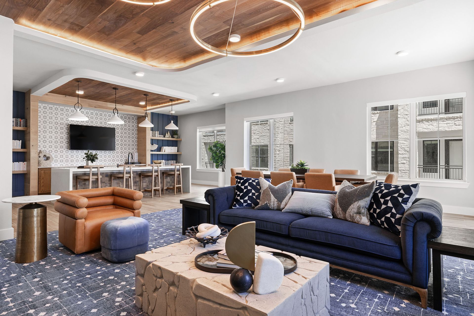 Spacious, modern lounge with blue sofa, armchairs, and dining area at The Wyatt, offering luxury apartments Cedar Park. Wood ceiling and terrazzo flooring.
