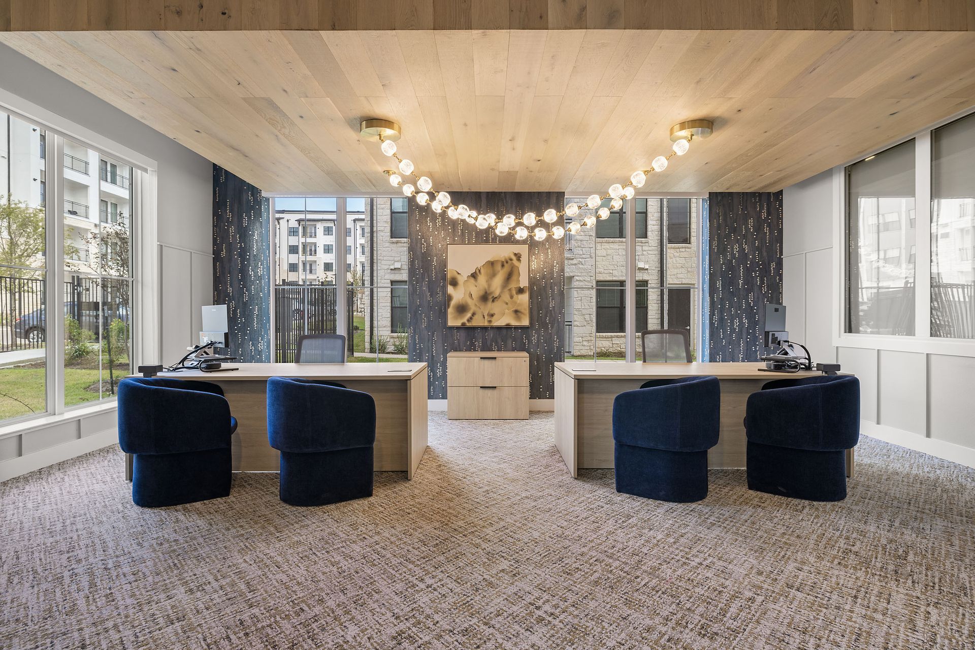 Two desks with blue chairs in a light-filled office at The Wyatt, offering apartments for rent in Austin, TX. Modern decor with a unique light fixture.