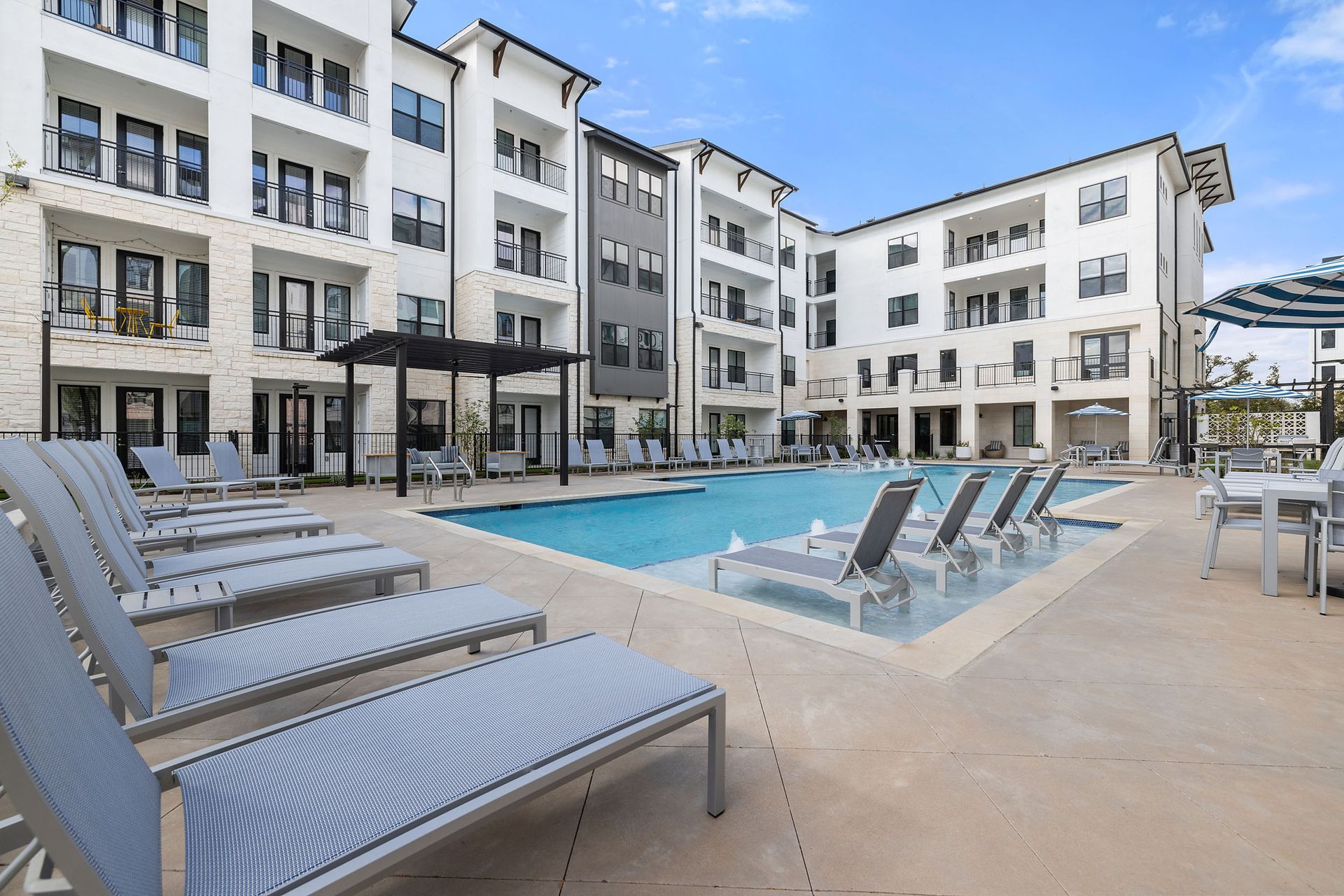 Swimming pool with lounge chairs, surrounded by a modern apartment complex on a sunny day at The Wyatt, offering Cedar Park luxury apartments.