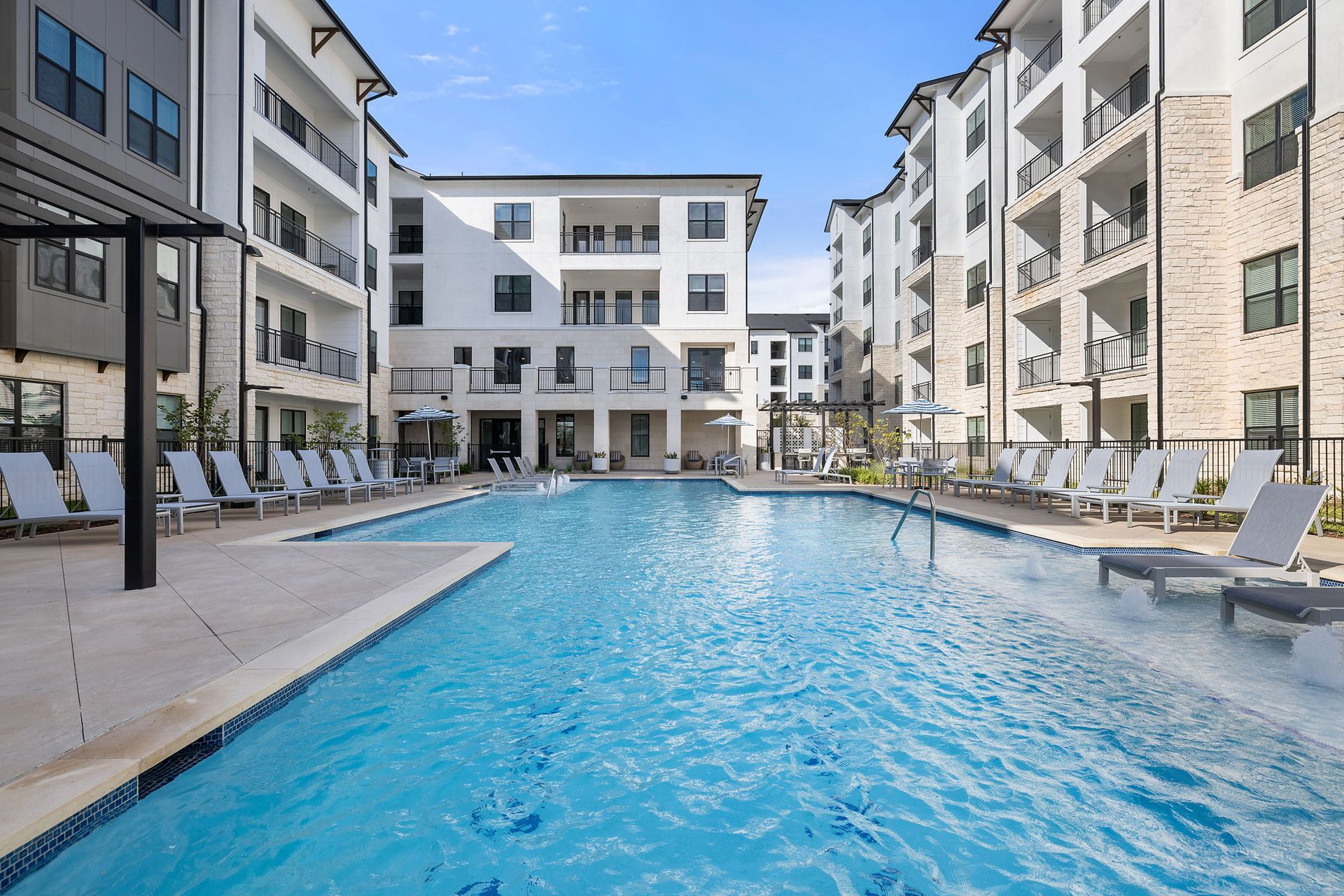 A large swimming pool surrounded by apartment buildings and lounge chairs at The Wyatt, offering luxury apartments Cedar Park. Bright, sunny day.
