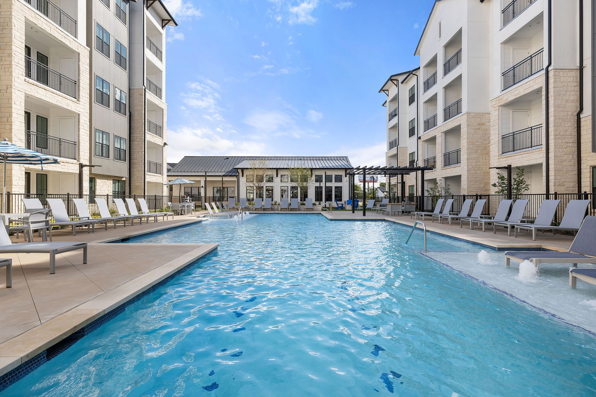 Swimming pool between apartment buildings on a sunny day with lounge chairs at The Wyatt, offering luxury apartments Cedar Park.
