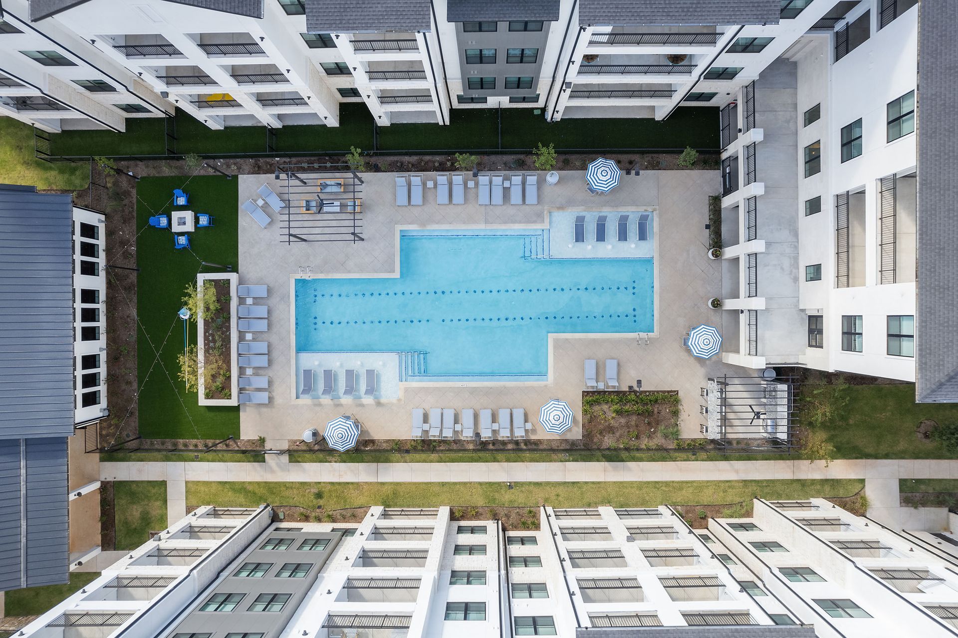 Overhead view of an apartment complex pool with lounge chairs, umbrellas, and grassy areas at The Wyatt, offering Cedar Park luxury apartments.