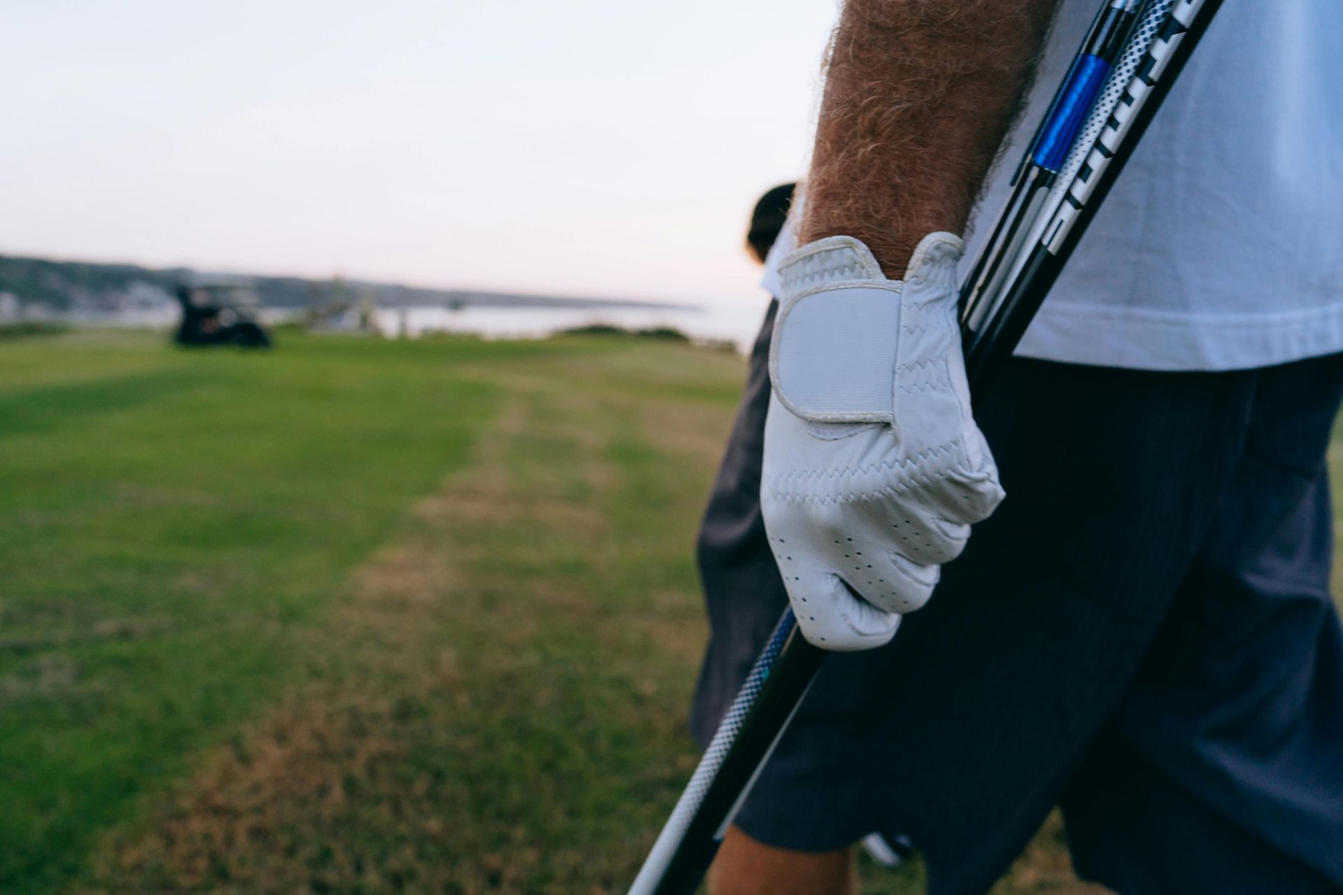 Golfer holding a club, wearing a white glove, on a green golf course.